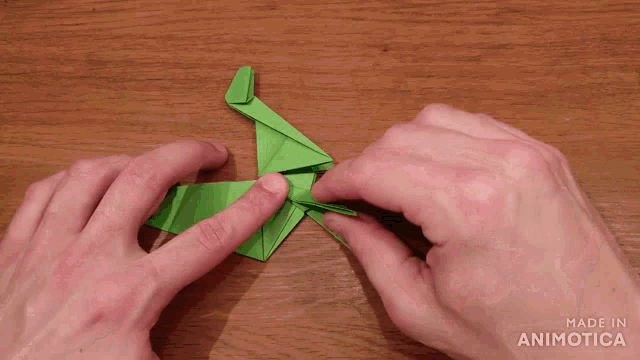 a person is making a green origami horse with the words made in animotica visible in the corner