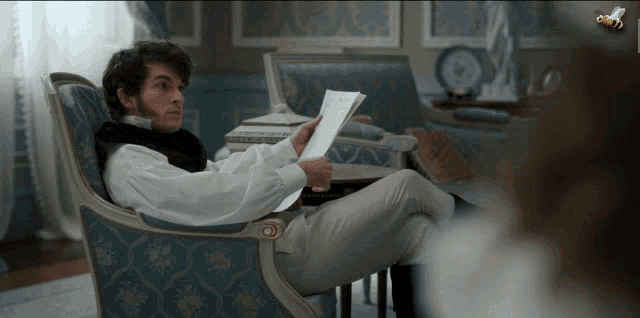 a man sits in a chair reading a letter with a bee on the wall behind him