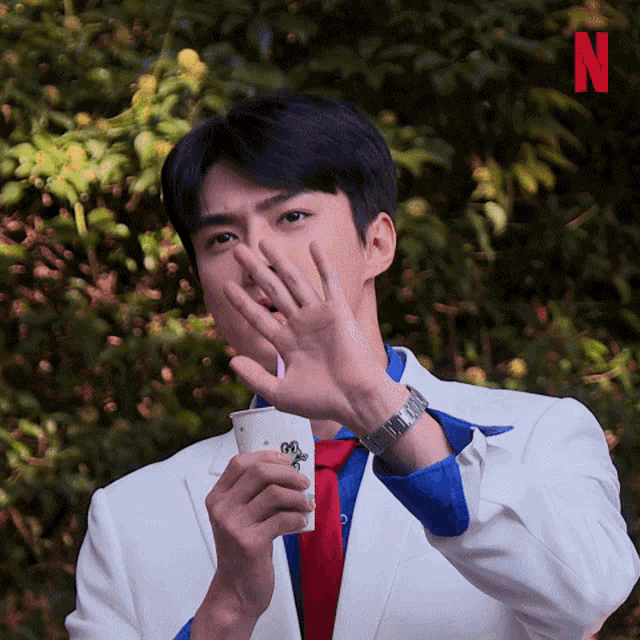 a man in a suit and tie covering his mouth while holding a cup with the letter n on it