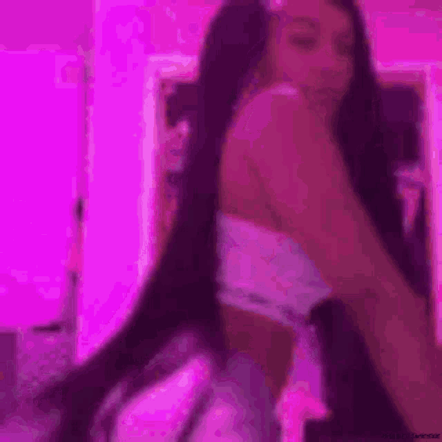 a woman with long black hair is standing in front of a mirror in a pink room .
