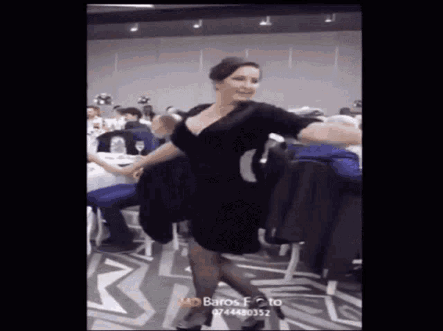 a woman in a black dress is dancing in a room full of people