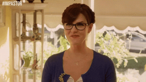 a woman wearing glasses and a blue cardigan is standing in front of a window with the hashtag #impastor above her