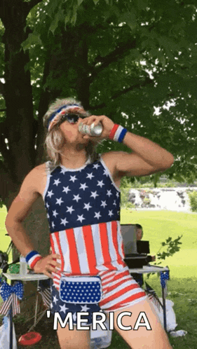 a man in an american flag outfit is drinking from a can while standing in front of a tree .