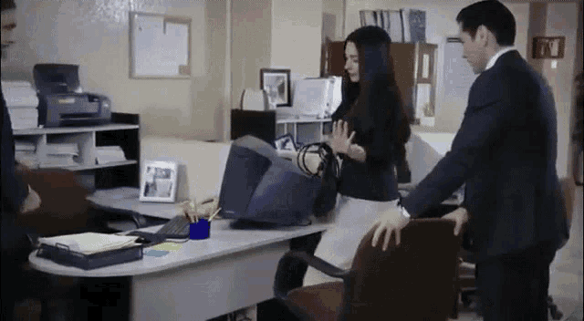 a man and a woman are standing in an office with a printer on the wall