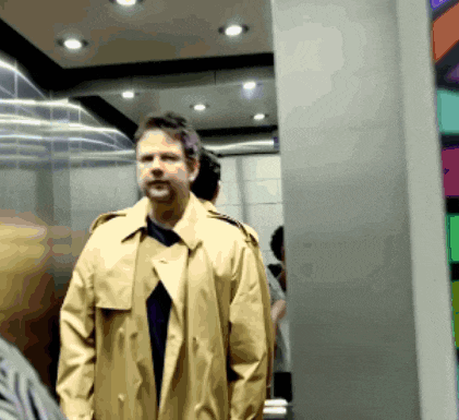 a man in a trench coat is standing in a elevator