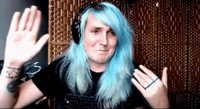 a woman with blue hair wearing headphones is waving her hand