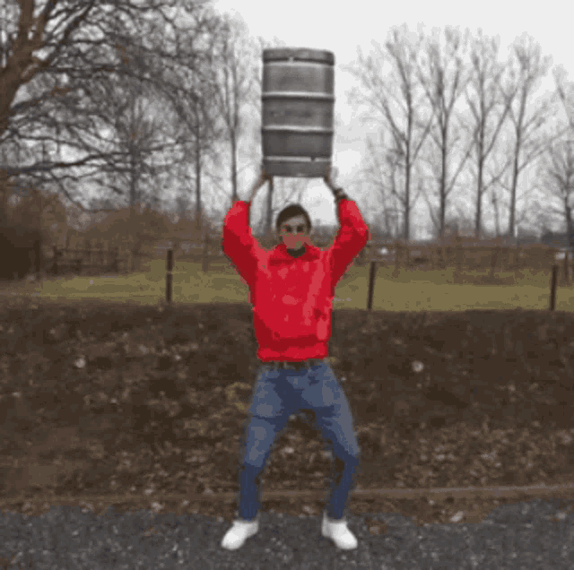 a man in a red sweatshirt is holding a large barrel over his head