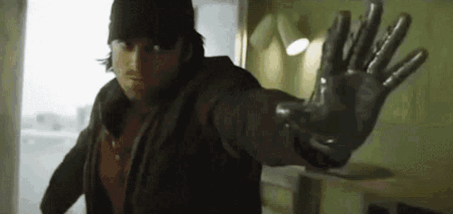a man wearing a black hat and a black glove is standing in a room with his arms outstretched .