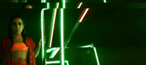 a woman in an orange top and red shorts is standing in front of a neon sign .