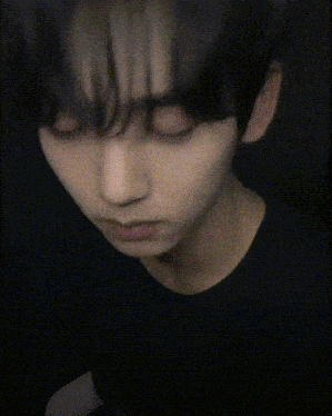 a close up of a young man 's face in a black shirt in a dark room .