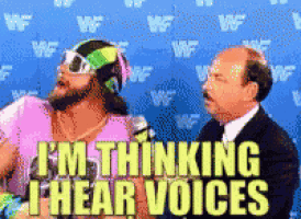 a man in a pink shirt is talking into a microphone while another man in a suit looks on