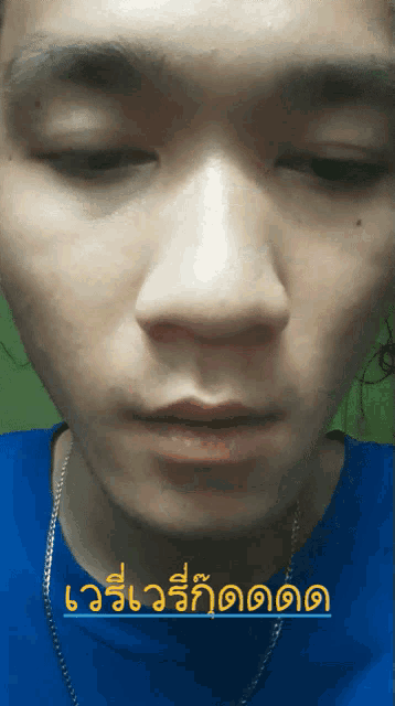 a close up of a man 's face with a blue shirt and a chain around his neck