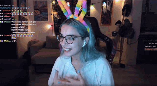 a woman wearing glasses and a rainbow colored headband is smiling on a screen