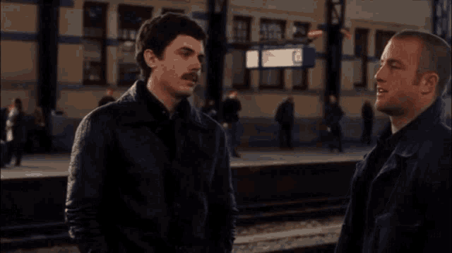 a man with a mustache talks to another man