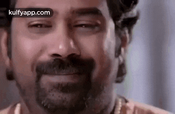 a man with a beard is smiling with his eyes closed and a necklace around his neck .