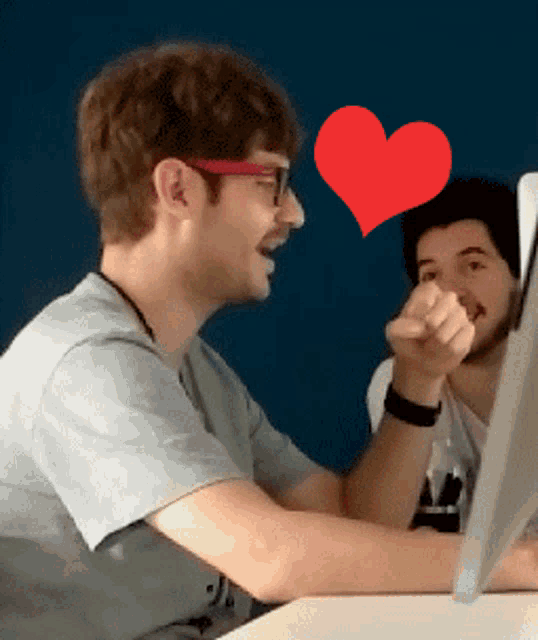 two men are sitting at a desk with a red heart above them