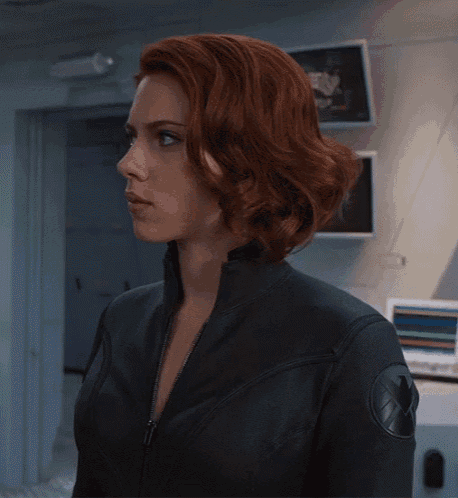 a woman with red hair is wearing a black jacket with a shield on the back