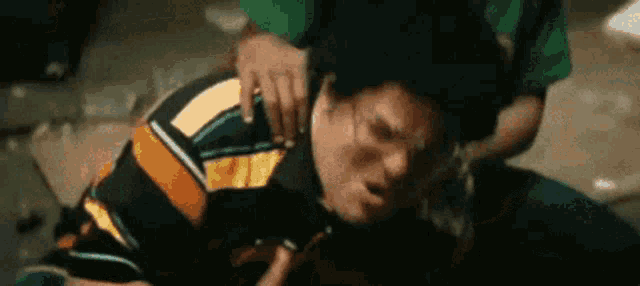 a man in a striped shirt is laying on the ground while a man in a green shirt holds his neck .