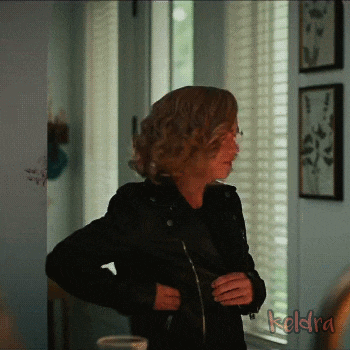 a woman in a black leather jacket is standing in front of a window with the word kedra written on the bottom
