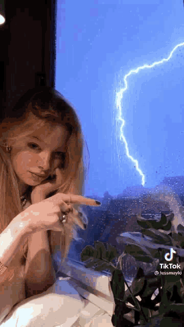 a young woman is pointing at a lightning bolt in the sky .