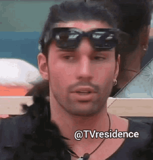 a man wearing sunglasses and a ponytail looks at the camera .
