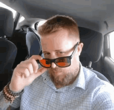 a man with a beard is wearing sunglasses while sitting in the back seat of a car .