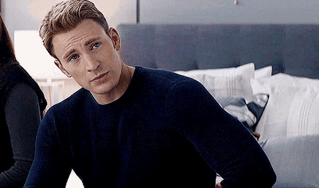 captain america is wearing a blue sweater and sitting on a bed .
