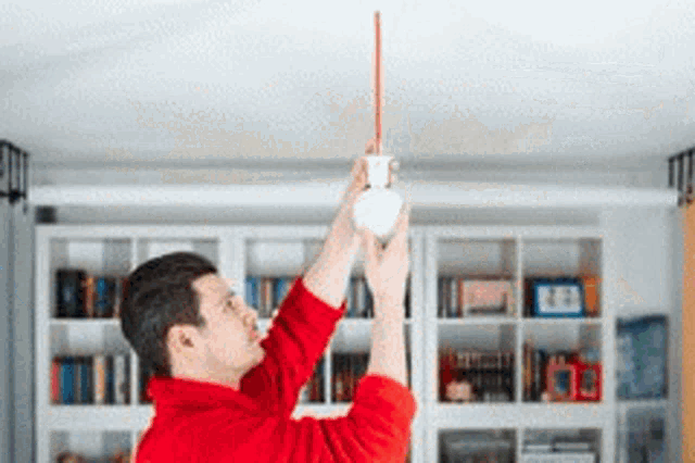 a man in a red sweater is hanging a light bulb from a ceiling .