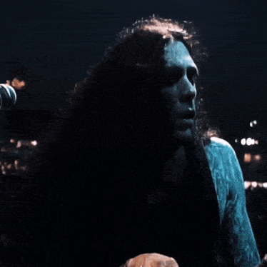 a man with long curly hair sings into a microphone