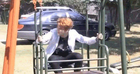 a man with red hair is sitting on a swing set in a park .