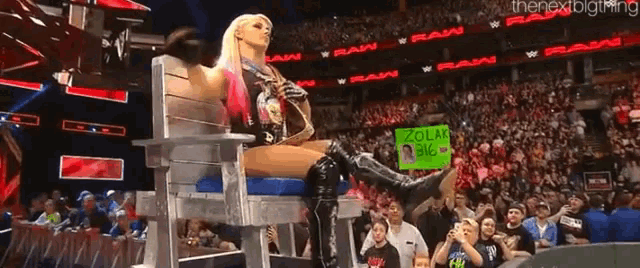 a woman is sitting in a chair in front of a crowd holding a sign that says " zola "