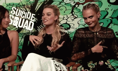 three women are sitting in front of a wall that says suicide squad on it