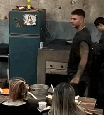 a man is standing in a kitchen with a group of people sitting at a table .