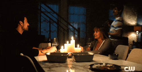 a couple sitting at a table with candles and a cw logo