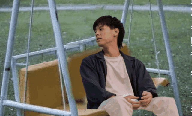 a young man is sitting on a yellow swing holding a remote control