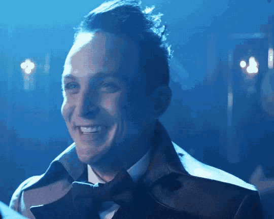 a man wearing a trench coat and bow tie smiles in a dark room