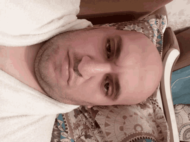 a bald man is laying on a bed with a white towel around his neck