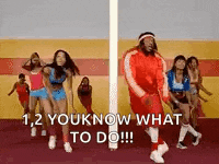 a group of people are dancing in a gym and a man is standing next to a pole .