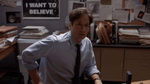a man sitting at a desk with a sign that says i want to believe