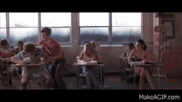 a group of people are sitting at desks in a classroom with a skeleton in the background .