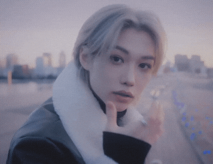 a young man with blonde hair and a white fur collar is standing in front of a city .