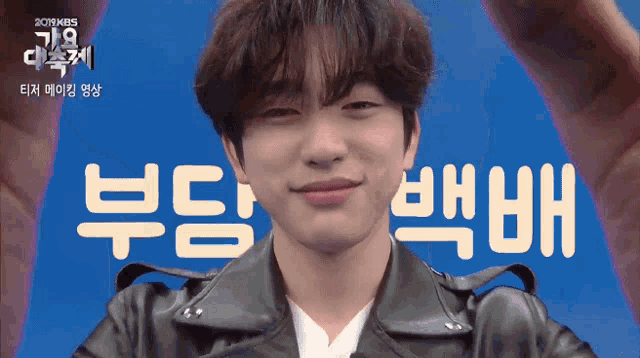 a man wearing a black leather jacket stands in front of a blue background with chinese writing on it
