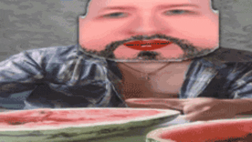 a man with a beard is sitting at a table eating watermelon