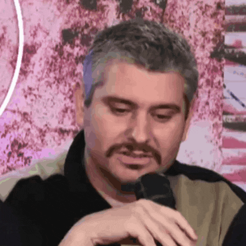 a man with a mustache is sitting in front of a microphone and making a funny face .
