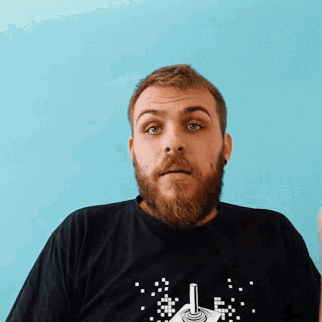a man with a beard is wearing a black t-shirt with an atari joystick on it