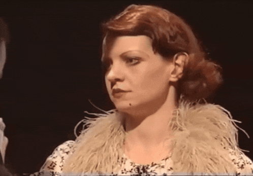 a woman with red hair and a fur collar looks at the camera