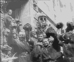 a black and white photo of a group of people standing in front of a building holding their hands up in the air .