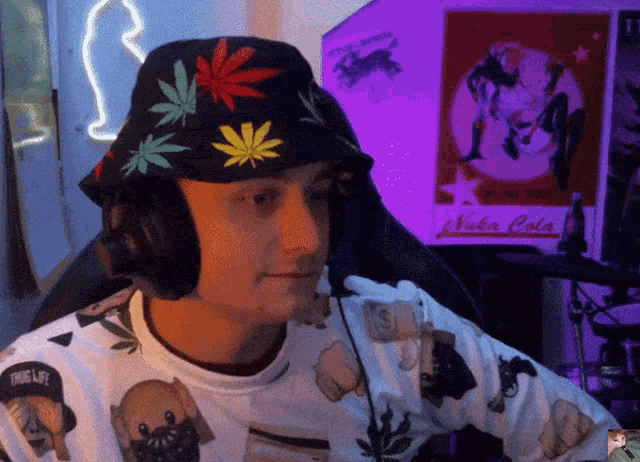 a man wearing a hat with marijuana leaves on it sits in front of a sign that says nuka cola