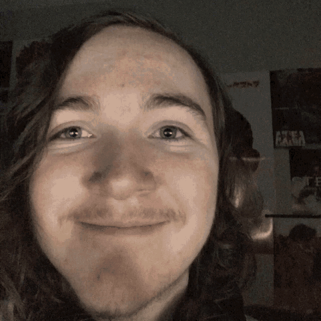 a man with long hair and a beard smiles in front of a wall with posters on it including one that says akira