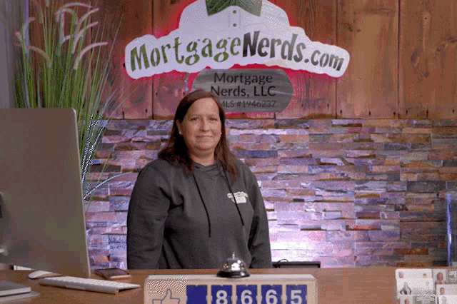 a woman stands at a desk in front of a sign for mortgage nerds llc